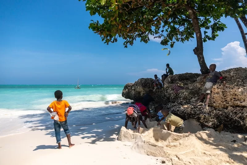 Children playing on the coral rocks at the end of Kendwa beach, Zanzibar, with the Indian Ocean behind them