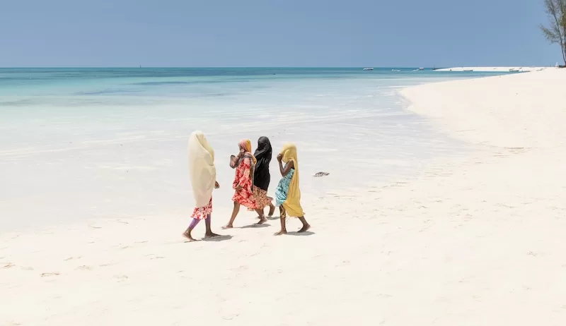Four women walking along the wide white sand at Kendwa, Zanzibar, with the Indian Ocean still in behind them