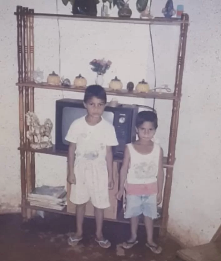 A faded childhood photograph of two boys standing in front of a shelf with an old television set