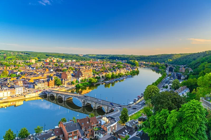 A stone bridge over a river bend through a Belgian town, seen from the citadel above