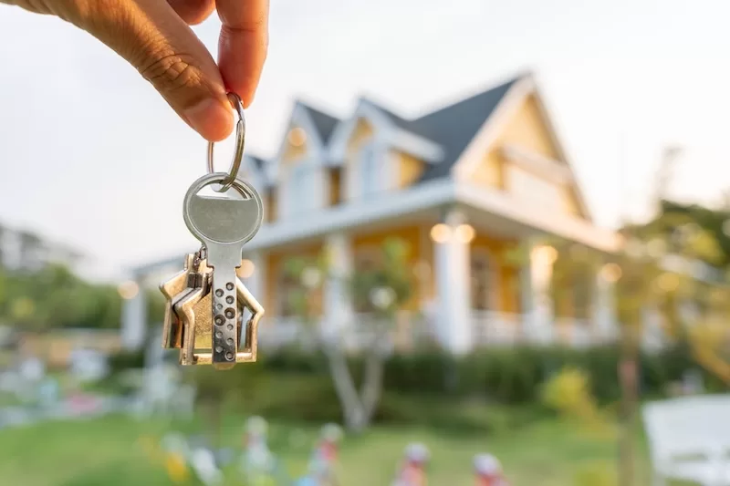 A hand holding house keys outside a family home, the kind of asset most people only think to protect once it is too late.