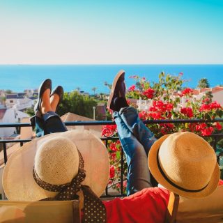 A couple relax on a balcony above whitewashed houses and the sea, the life the Spain non-lucrative visa is built for