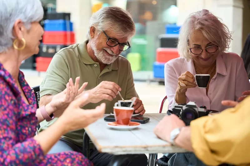 Three retirees laugh over espresso at a café table.