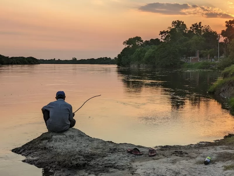 A man fishes from a riverbank at sunset on a wide, quiet river: the unhurried world a Paraguay residency belongs to.