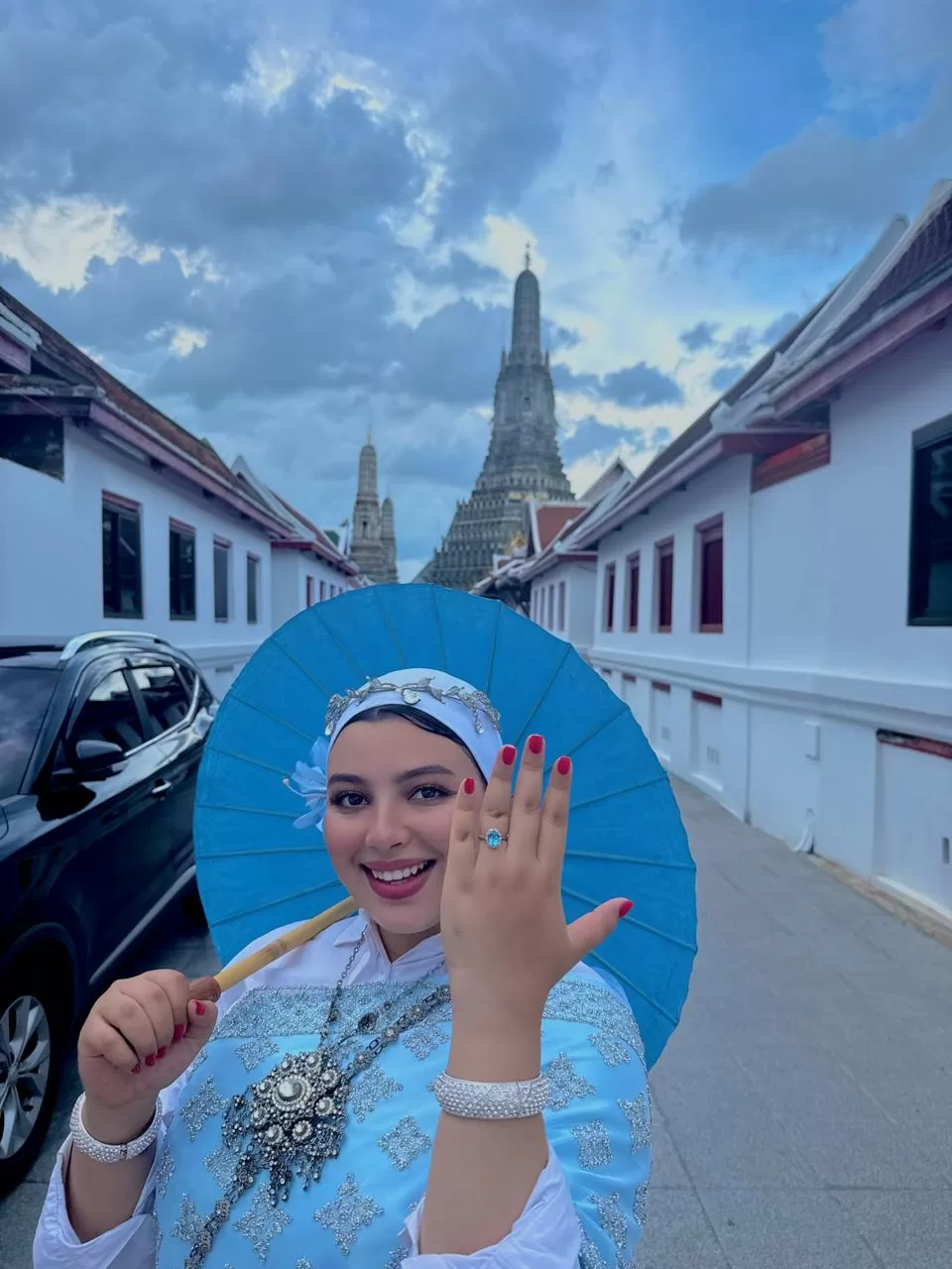 Anis’s wife in a rented Thai dress and parasol shows her ring, with Wat Arun rising behind.