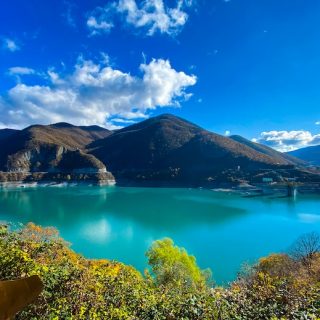 A turquoise mountain reservoir under a bright blue sky, ringed by autumn hillsides.