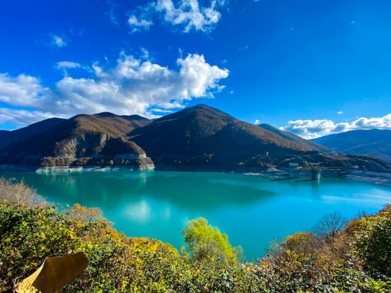 A turquoise mountain reservoir under a bright blue sky, ringed by autumn hillsides.
