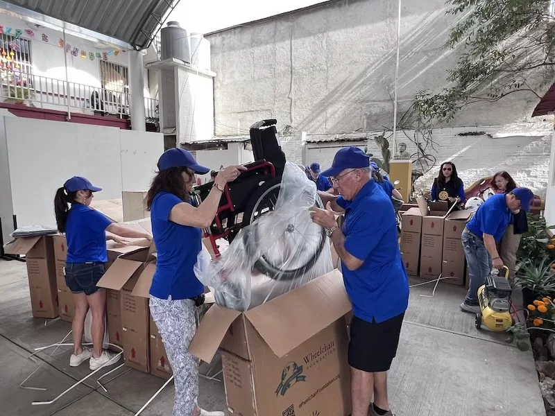 Volunteers in blue shirts unbox and assemble wheelchairs in a courtyard.