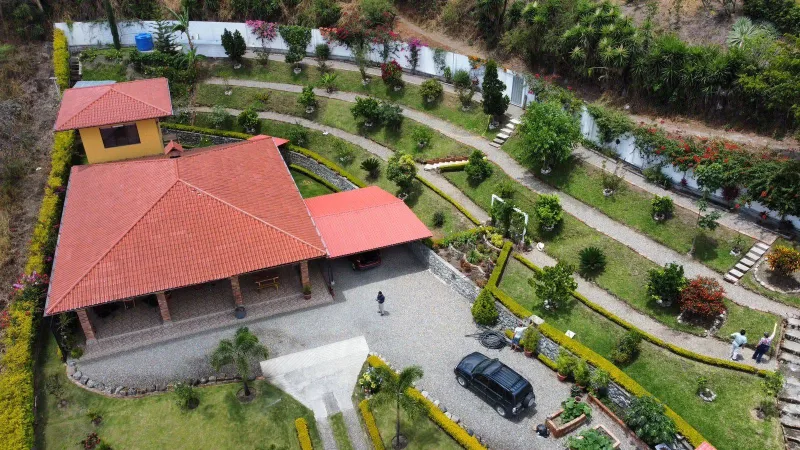 Aerial view of Casa Libélula, a red-roofed home with terraced gardens in the Malacatos Valley, the finished result of building a house in Ecuador.