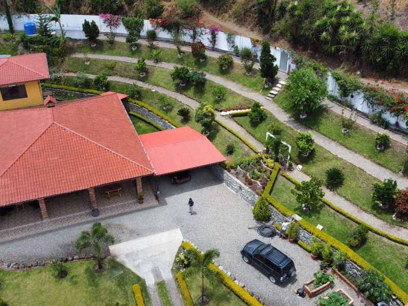 Aerial view of Casa Libélula, a red-roofed home with terraced gardens in the Malacatos Valley, the finished result of building a house in Ecuador.