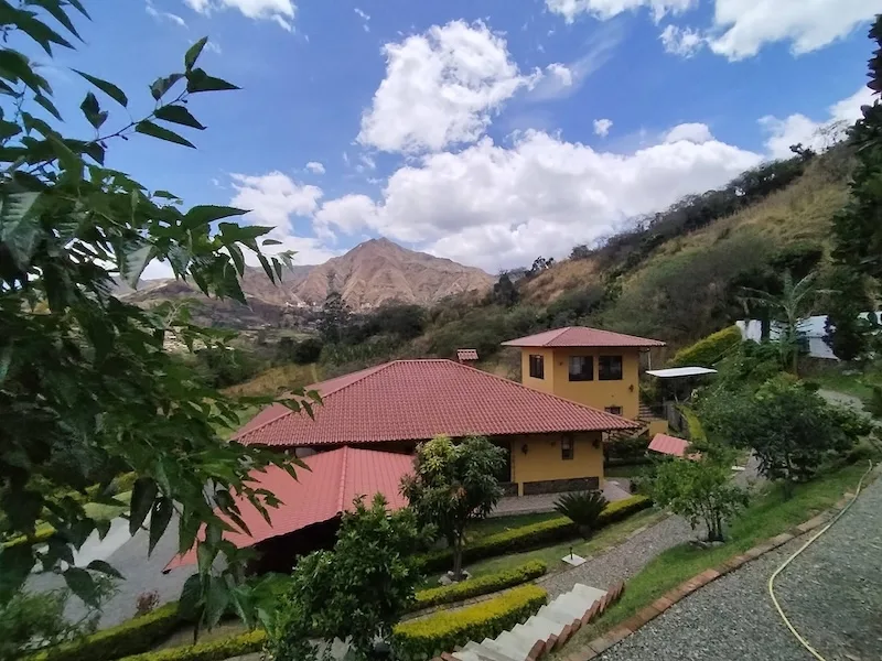 Casa Libélula finished, a yellow house with a red tile roof and garden paths below a rocky peak.