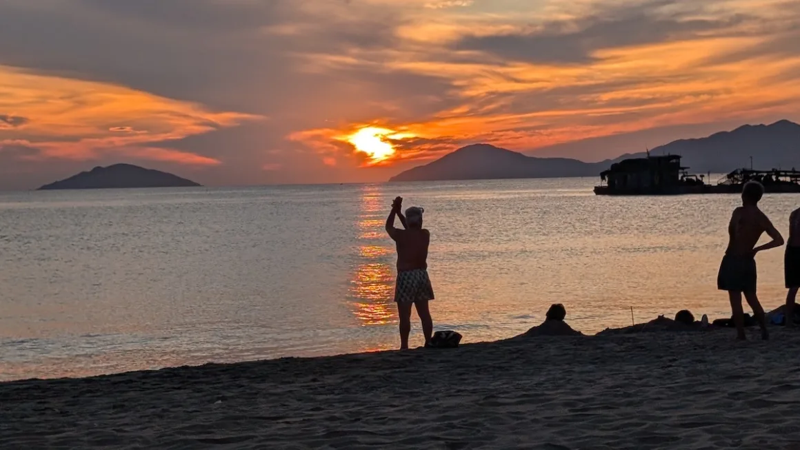 People on the sand watch the sun set over the sea and islands off central Vietnam.