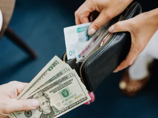 Hands exchanging US dollar bills, the currency that now buys about 24% fewer Costa Rican colones than in 2023