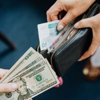 Hands exchanging US dollar bills, the currency that now buys about 24% fewer Costa Rican colones than in 2023