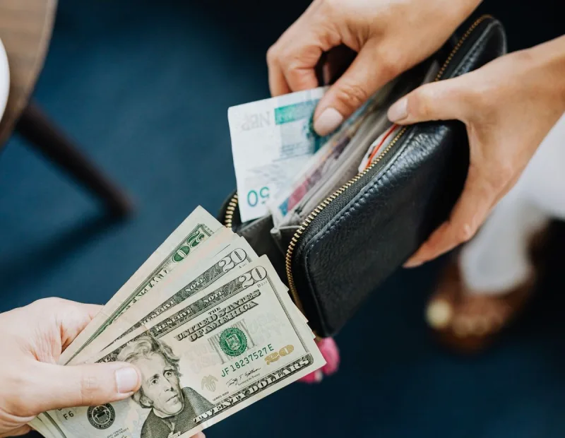 Hands exchanging US dollar bills, the currency that now buys about 24% fewer Costa Rican colones than in 2023