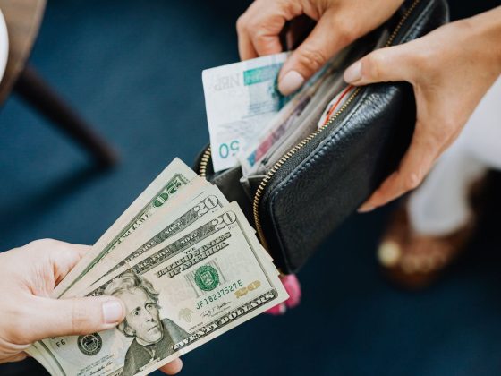 Hands exchanging US dollar bills, the currency that now buys about 24% fewer Costa Rican colones than in 2023