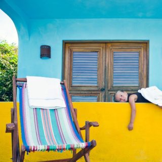 A young girl rests on a bright yellow balcony beside a striped deck chair.