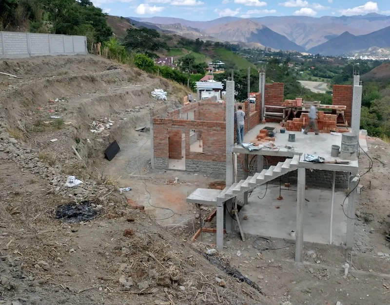 The brick house under construction on its hillside lot, with the valley and mountains beyond.