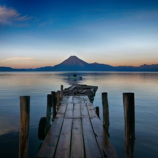 A weathered wooden dock reaches into still water at dawn, a volcano on the far shore: the view that sells living in Lake Atitlán