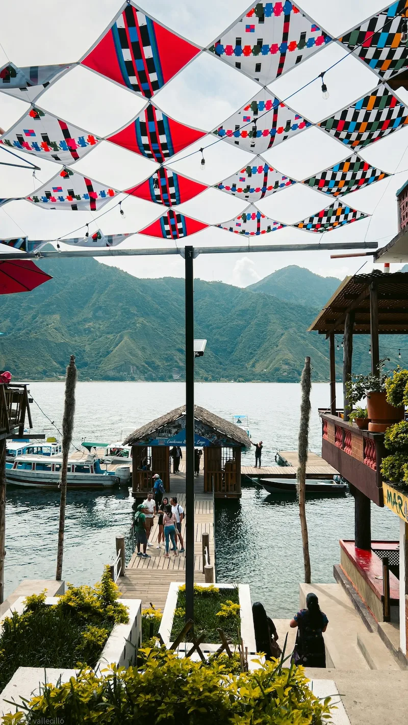 Maya textile-patterned canopies shade a village path down to a boat pier on the lake.