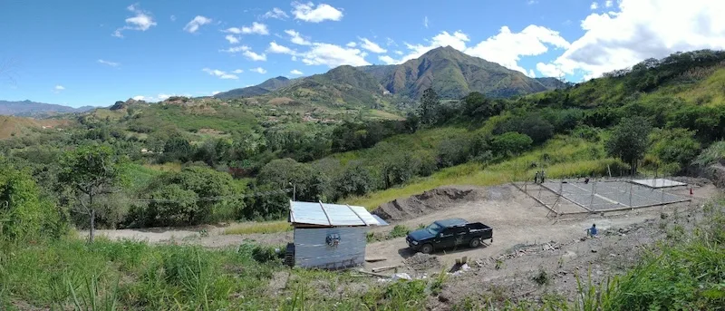The bare hillside plot in the Malacatos Valley before building began, with green mountains behind.