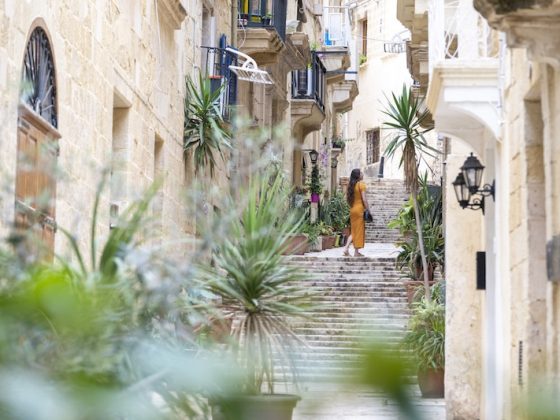 A woman in a yellow dress walks up a plant-lined limestone street in Malta, the country facing the first of the expat rule changes 2027 brings