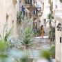 A woman in a yellow dress walks up a plant-lined limestone street in Malta, the country facing the first of the expat rule changes 2027 brings