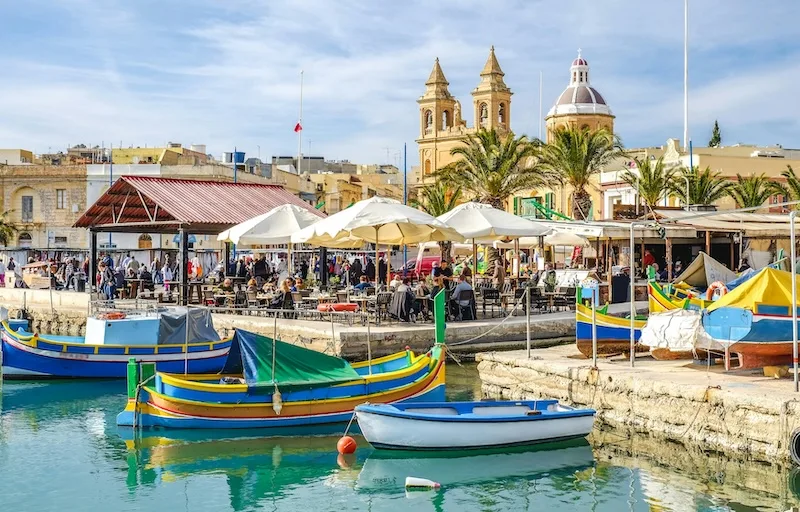Colorful luzzu fishing boats moored in Marsaxlokk harbor, Malta.