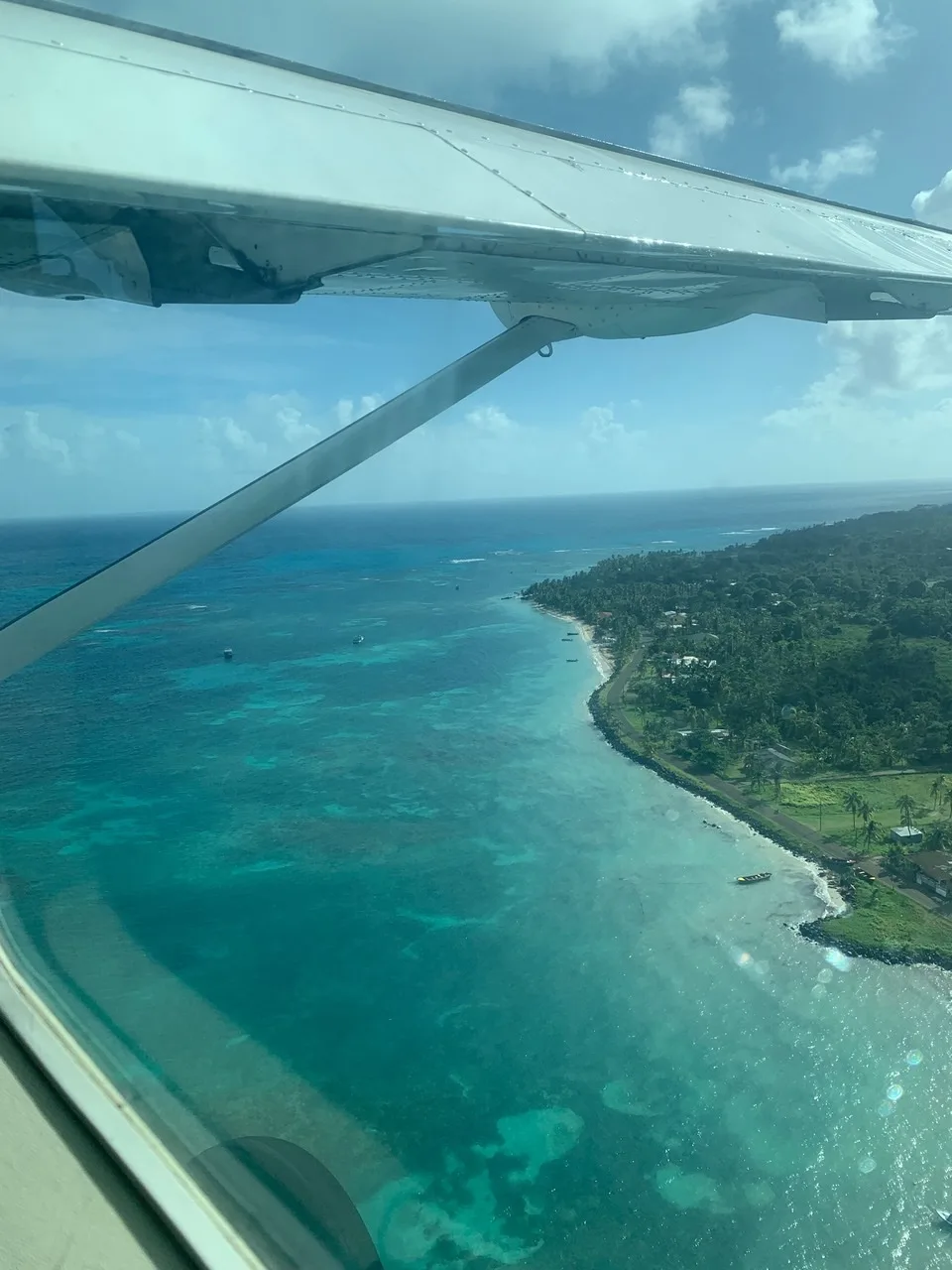 The view from a small plane over a turquoise reef and a palm-lined island coast.