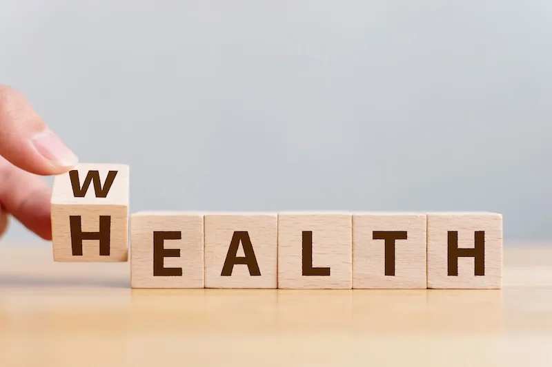 A hand turns a wooden block to change the word WEALTH into HEALTH.