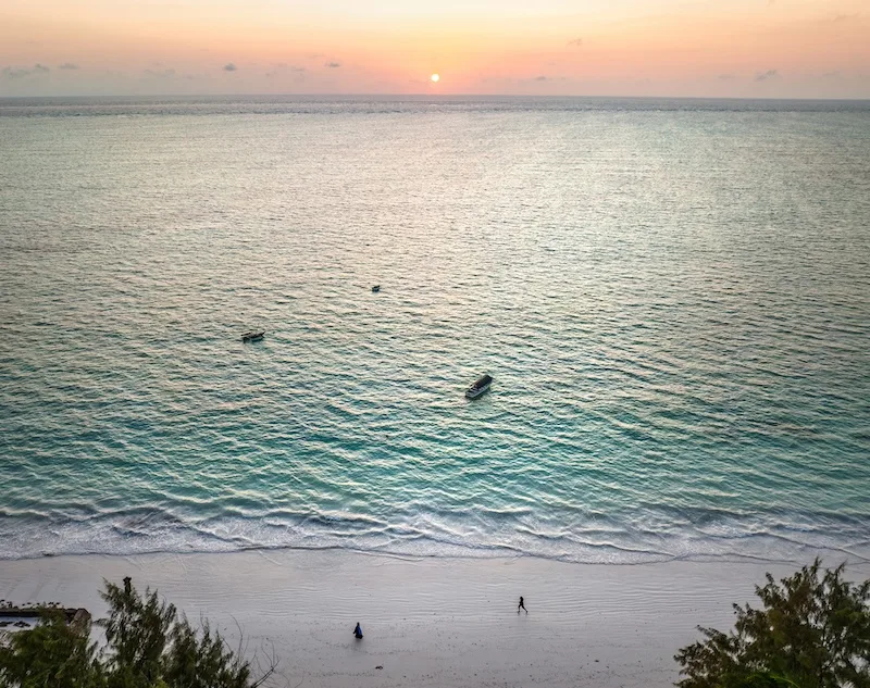 Sunset over the Indian Ocean seen from above a quiet Zanzibar beach, with fishing boats anchored offshore